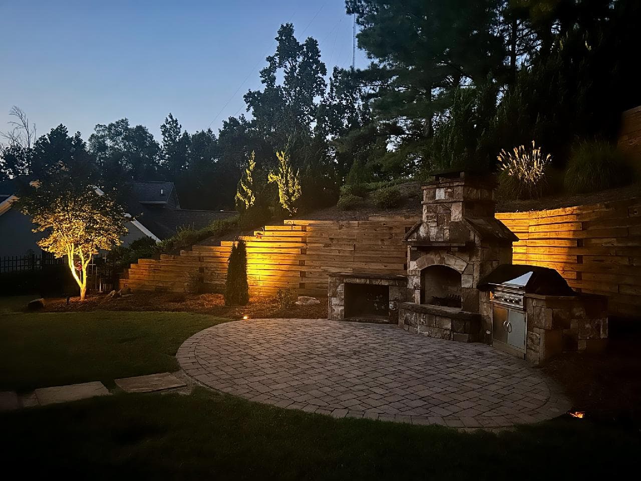 Outdoor fireplace and patio lit with energy-efficient LED landscape lighting at night