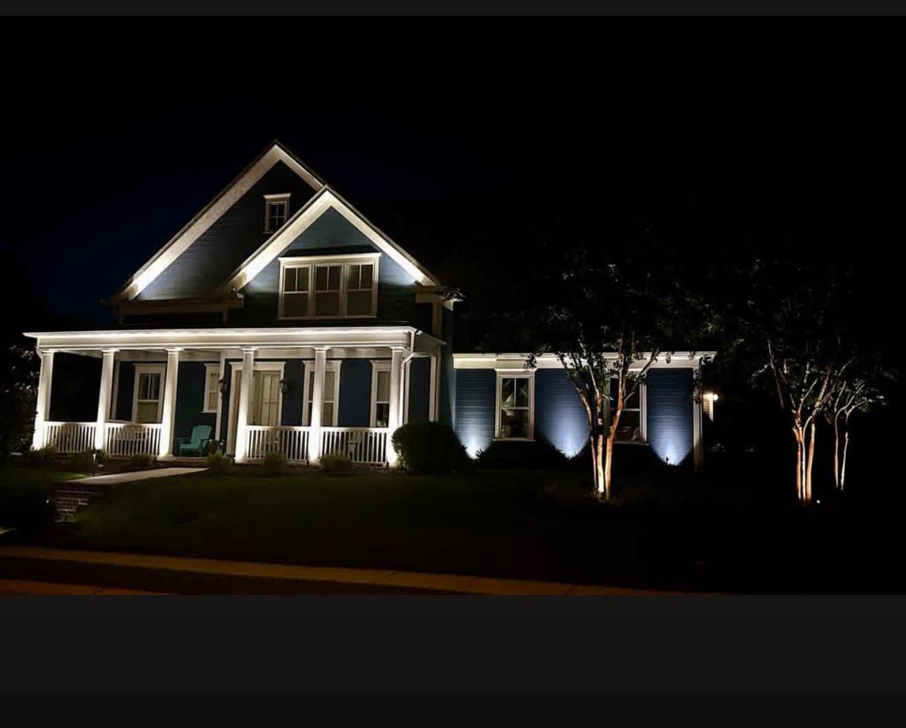 Two-story home with dramatic facade uplighting and accented trees at night