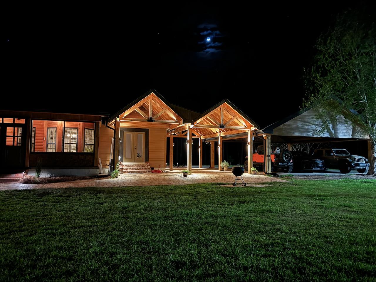 Craftsman cabin with twin timber-frame gabled porches glowing warmly under a moonlit sky