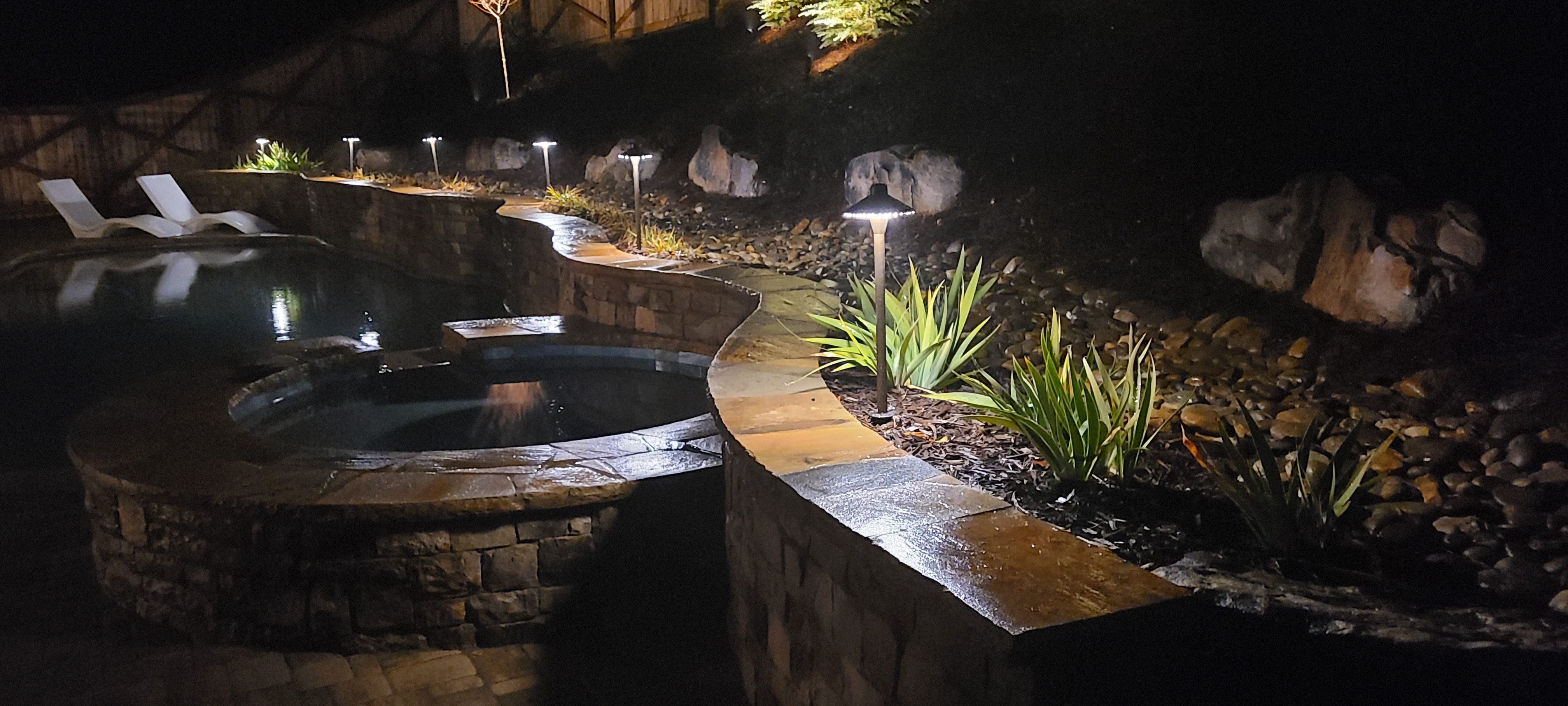 Backyard pool and spa with stone coping, flagstone path, and warm landscape path lighting at night